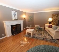 Elegant living room featuring a white fireplace, hardwood floors, beige sofa, patterned rug, and wall sconces, with neutral toned walls adorned with artwork.