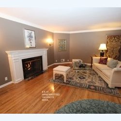 Elegant living room featuring a white fireplace, hardwood floors, beige sofa, patterned rug, and wall sconces, with neutral toned walls adorned with artwork.