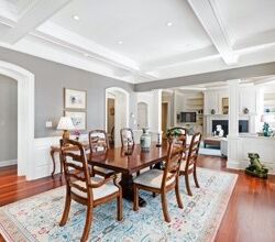 Elegant dining room with wooden table set for six, ornate chairs, white walls, hardwood floors, and a view into adjacent rooms.