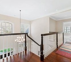 Bright hallway with arched window, dark wooden railing, white walls, and a colorful striped rug on hardwood floor.