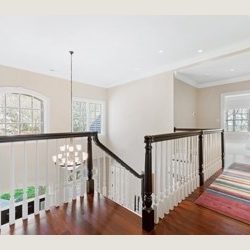 Bright hallway with arched window, dark wooden railing, white walls, and a colorful striped rug on hardwood floor.